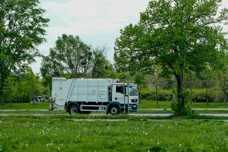 Camion poubelle blanc sur route entourée de verdure